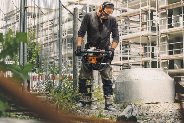 Mann benutzt STIHL BT 131 Erdbohrgerät auf Baustelle mit Schutzausrüstung