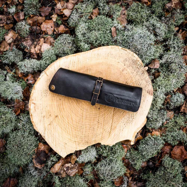 Schwarze Petromax Leder-Bestecktasche auf Holzstumpf in moosigem Wald