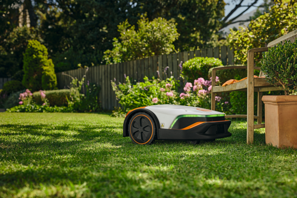 STIHL iMOW 7 Mähroboter im Einsatz auf einem grünen Rasen in einem blühenden Garten