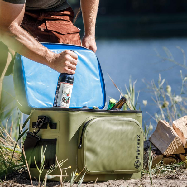 Person holt Flasche aus Petromax Kühlbox am Seeufer