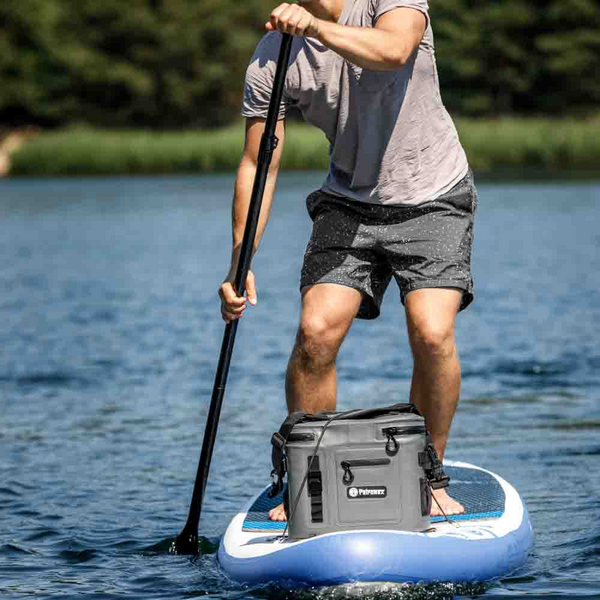 Mann auf SUP mit Petromax Kühlbox auf ruhigem Gewässer bei Sonnenschein