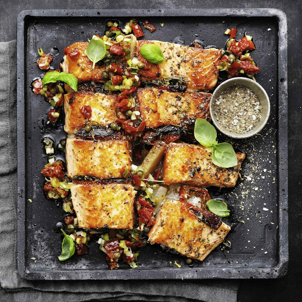 Gegrillter Lachs auf schwarzer Platte mit Tomaten, Kapern, Oliven und Basilikum