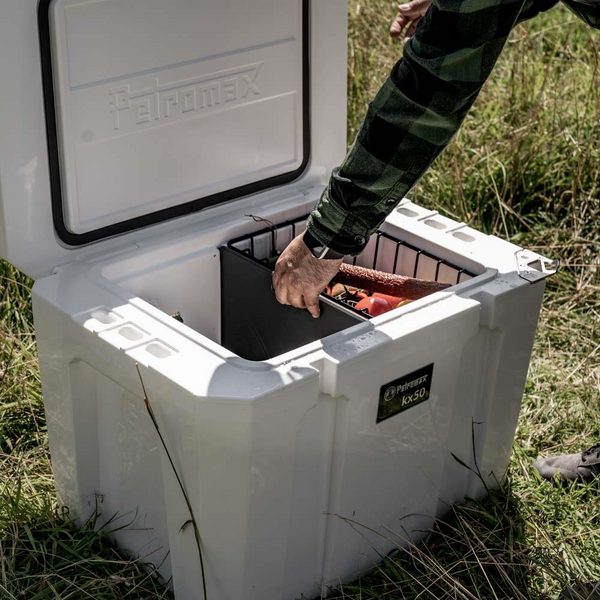 Person setzt Schneidebrett in Petromax Kühlbox ein, draußen mit Lebensmitteln darauf