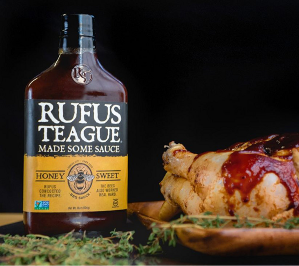 Flasche Rufus Teague Honey Sweet BBQ Sauce neben gegrilltem Hähnchenbein