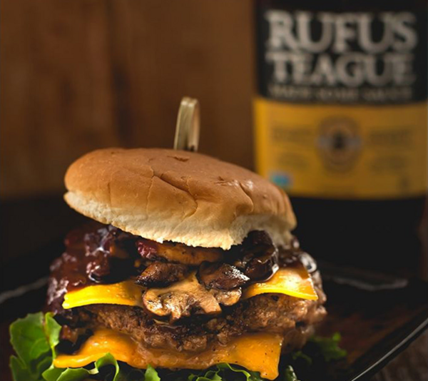 Burger mit Käse und Rufus Teague BBQ Sauce auf Holztisch