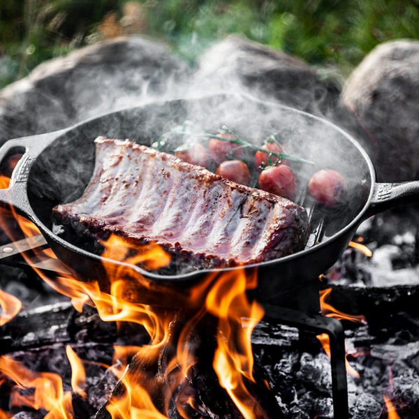 Petromax Gusseisenpfanne auf offenem Feuer mit Fleisch und Tomaten