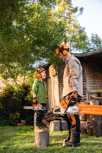 Erwachsener und Kind mit STIHL Helmen und Motorsägen im Garten