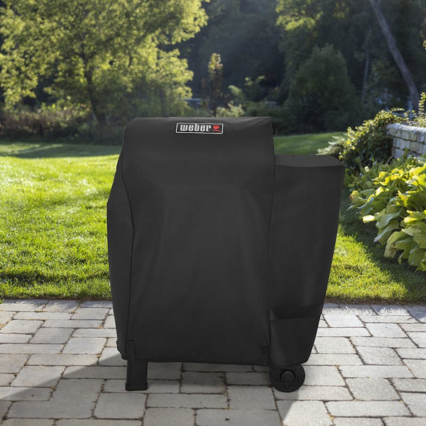Weber Premium Abdeckhaube über einem Searwood Holzpelletgrill im sonnigen Garten