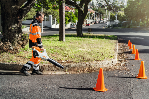 Mann in Sicherheitskleidung benutzt Stihl Akku-Laubbläser auf städtischer Straße