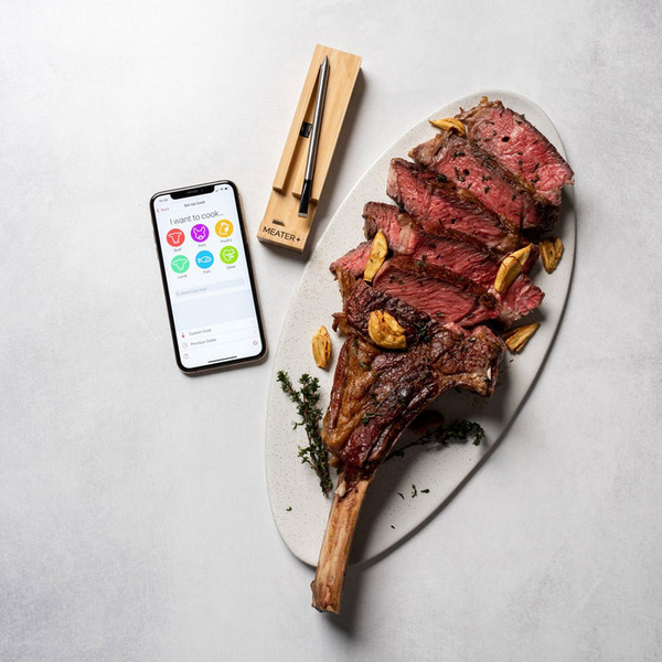 Smartphone mit App neben Tomahawk-Steak und MEATER Plus Thermometer