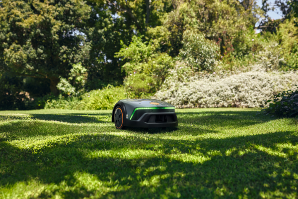 STIHL iMOW 4 EVO Mähroboter in Aktion auf sonnigem grünen Rasen mit Büschen im Hintergrund