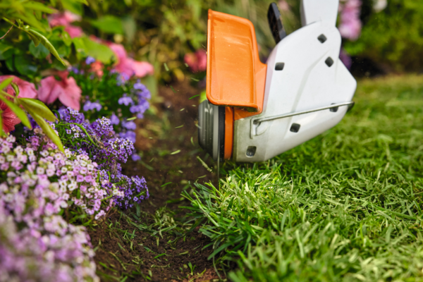 STIHL FSA 30 Akku-Motorsense im Einsatz, schneidet Gras nahe farbenfrohen Blumen im Garten