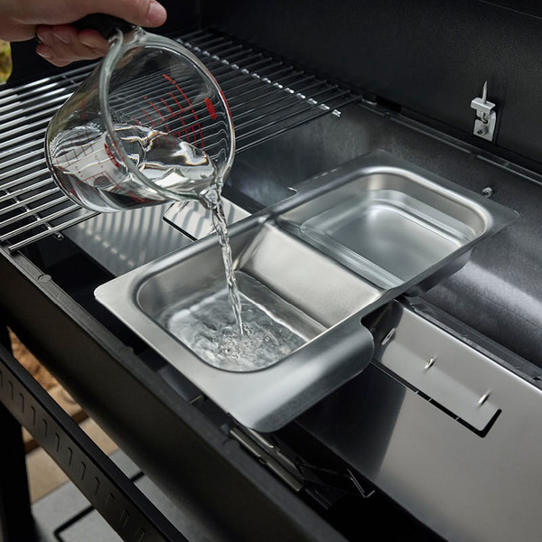 Person füllt Wasser in Weber Wet-Smoke-Set auf Searwood Grill