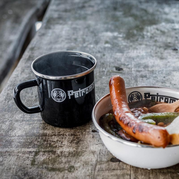 Schwarzer Petromax Emaille-Becher neben Schüssel mit Essen auf steinerner Oberfläche