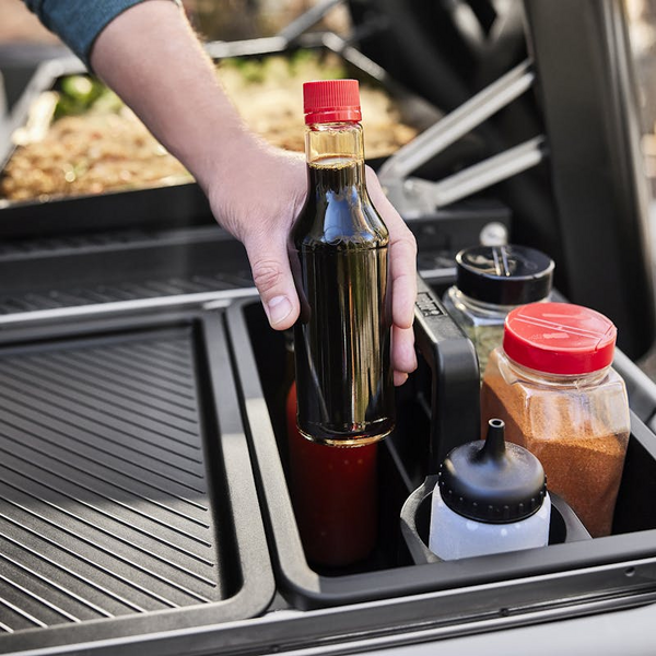 Hand hebt Flasche aus Weber Works Transportbehälter auf Grilltisch