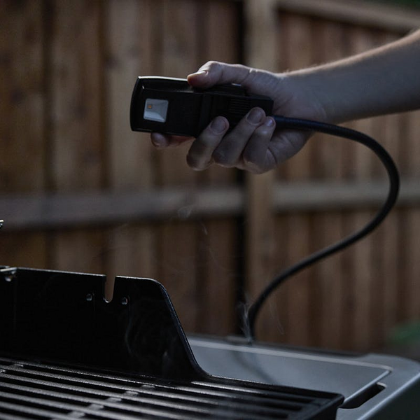 Hand hält flexible LED-Lampe über einem Grill bei Dämmerung