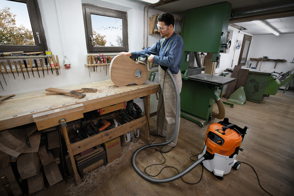 Mann in Tischlerwerkstatt bearbeitet Holz neben STIHL SE 122 E Sauger