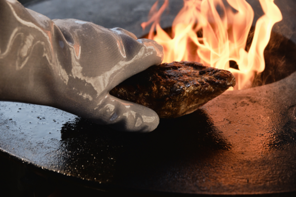Silikon-Grillhandschuh hält gegrilltes Fleisch auf heißer Platte nahe Flammen