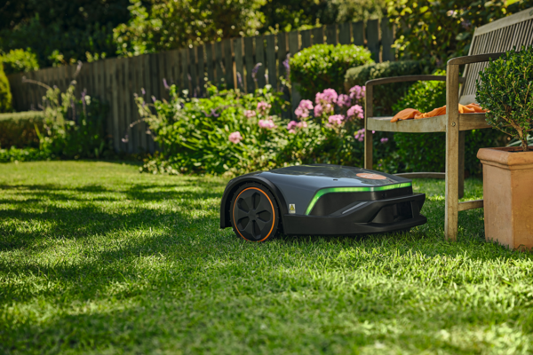 STIHL iMOW 5 EVO Mähroboter mäht Rasen in sonnigem Garten mit Blumen und Holzbank