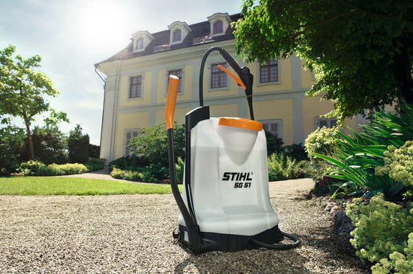 STIHL SG 51 Spritzgerät auf Kiesweg vor gelbem Herrenhaus im sonnigen Garten