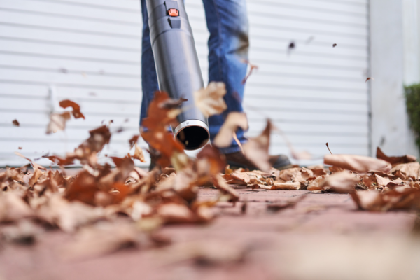 Person verwendet STIHL BGA 60 Akku-Laubbläser auf einem gepflasterten Weg vor einer Garagentür