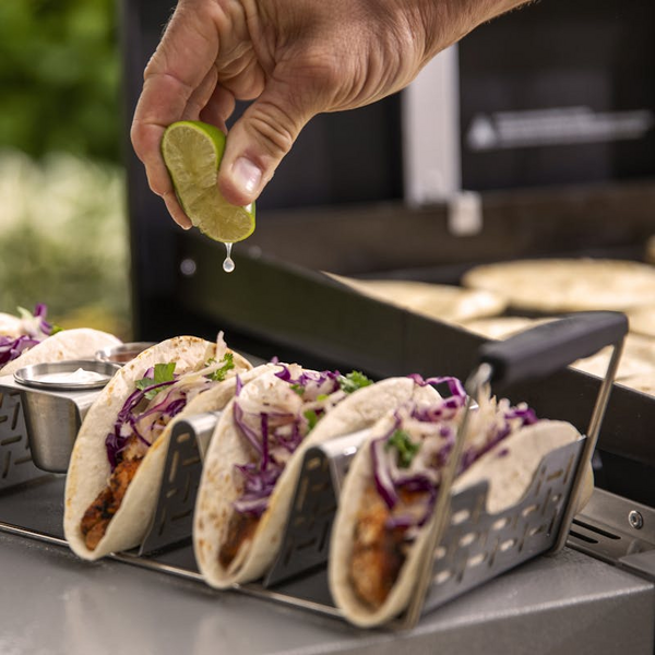 Hand drückt Limettensaft über gefüllte Tacos im Weber Taco Rack neben einem Grill
