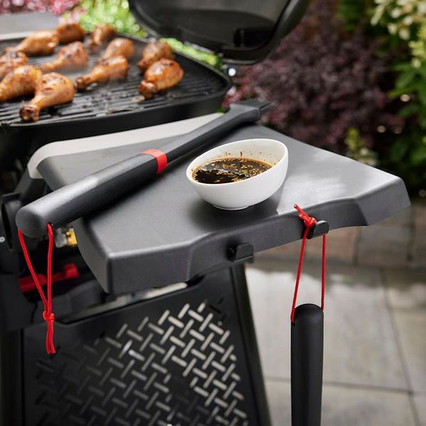 Weber Seitentisch mit Grillsoße und Hähnchen im Hintergrund