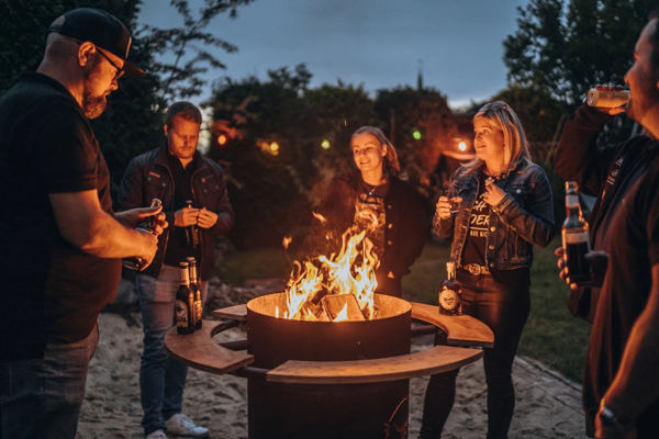 Gruppe von fünf Personen genießt geselliges Beisammensein um eine Feuerschale im Freien