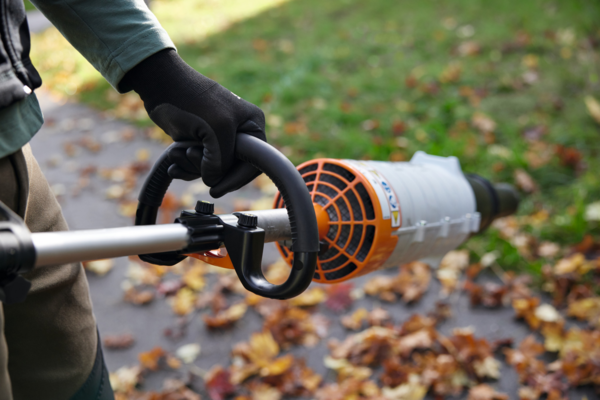 Person bedient Stihl KMA 120 R Akku-KombiMotor in herbstlichem Garten