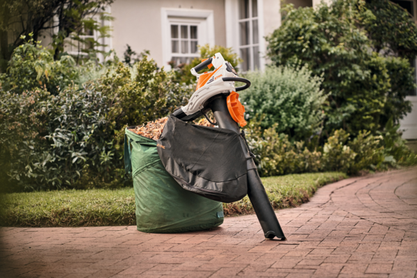 STIHL SHA 56 Akku-Saughäcksler auf einem Gartenweg neben einem gefüllten Fangsack