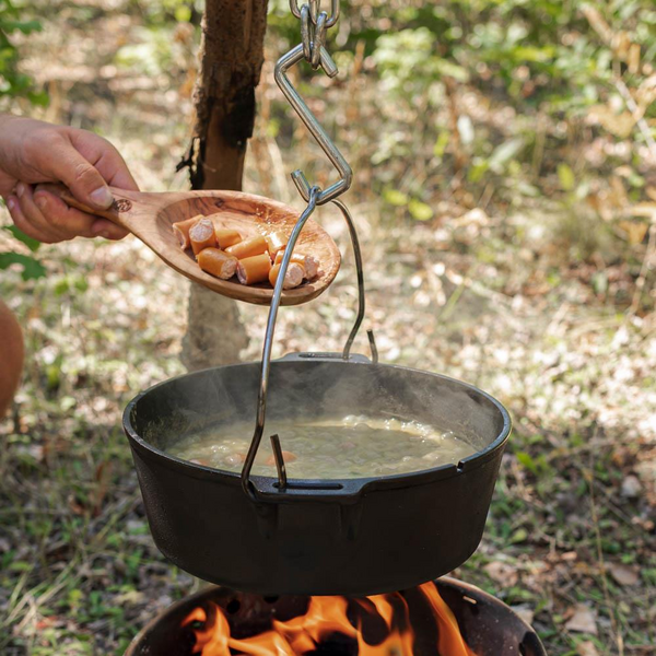 Person verwendet Petromax Olivenholz Griffschale zum Schöpfen von Essen aus einem Topf über Lagerfeuer