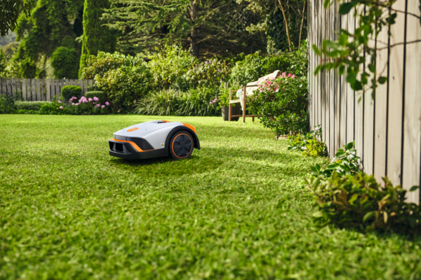 STIHL iMOW 4 Mähroboter mäht selbstständig einen grünen Rasen in einem schönen Garten