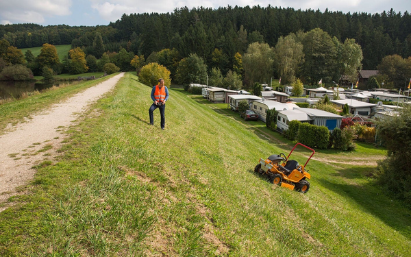 Mann bedient ferngesteuerten Aufsitzmäher AS 940 Sherpa auf Hang neben Campingplatz