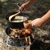 Person verwendet Petromax Olivenholzkelle beim Outdoor-Kochen über Lagerfeuer