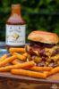 Burger mit Old Texas BBQ Sauce und Pommes auf Holzbrett im Freien