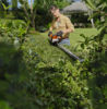 Frau benutzt STIHL HSA 60 Akku-Heckenschere in einem sonnigen Garten