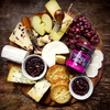 Käseplatte mit Stokes Red Onion Marmelade, Trauben, Äpfeln und Crackern auf Holzbrett
