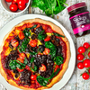 Pizza mit Stokes Red Onion Marmelade, Spinat, Tomaten und Oliven auf rustikalem Holztisch