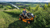 Mann bedient AS 940 Sherpa 4WD XL B&S Aufsitzmäher auf steiler Wiese mit Flussblick