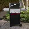 Weber SPIRIT E-325 GBS Gasgrill in einem Garten auf gepflastertem Weg