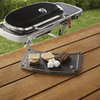 Weber Traveler Schneidebrett auf Holztisch mit S'mores Zutaten, Grill im Hintergrund