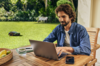 Mann arbeitet am Laptop im Garten mit STIHL Mähroboter im Hintergrund