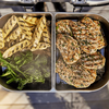 Geöffneter Elektrogrill mit Edelstahlschalen gefüllt mit gegrilltem Gemüse und Hähnchen