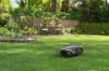 STIHL iMOW 3 EVO Mähroboter mäht Rasen in einem blühenden Garten mit Sitzbereich