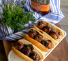 Drei Hotdog-Brötchen mit BBQ-Fleischbällchen und Rufus Teague Sauce im Hintergrund