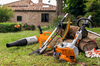 STIHL Gartengeräte inklusive KM 56 RC-E KombiMotor und Aufsätze auf Rasen vor Steinhaus