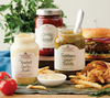 Stonewall Kitchen Saucen auf Schieferplatte mit Burger und Pommes im Hintergrund