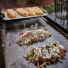 Weber Warmhalterost mit Brötchen über gegrilltem Fleisch und Gemüse auf einem Flat Top Grill