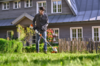 Mann benutzt STIHL FSA 50 Akku-Motorsense im Garten vor einem grauen Haus