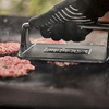Hand in hitzebeständigem Handschuh verwendet Weber Hamburgerpresse auf Grillplatte